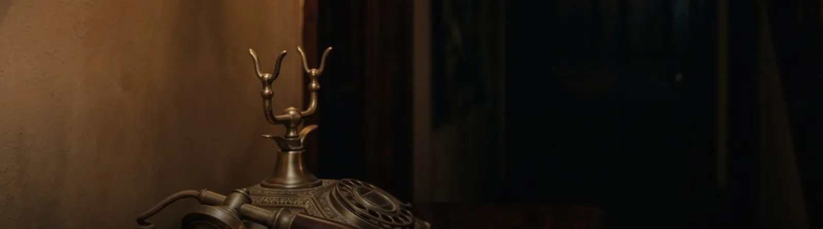 An antique brass telephone on a side table in low light